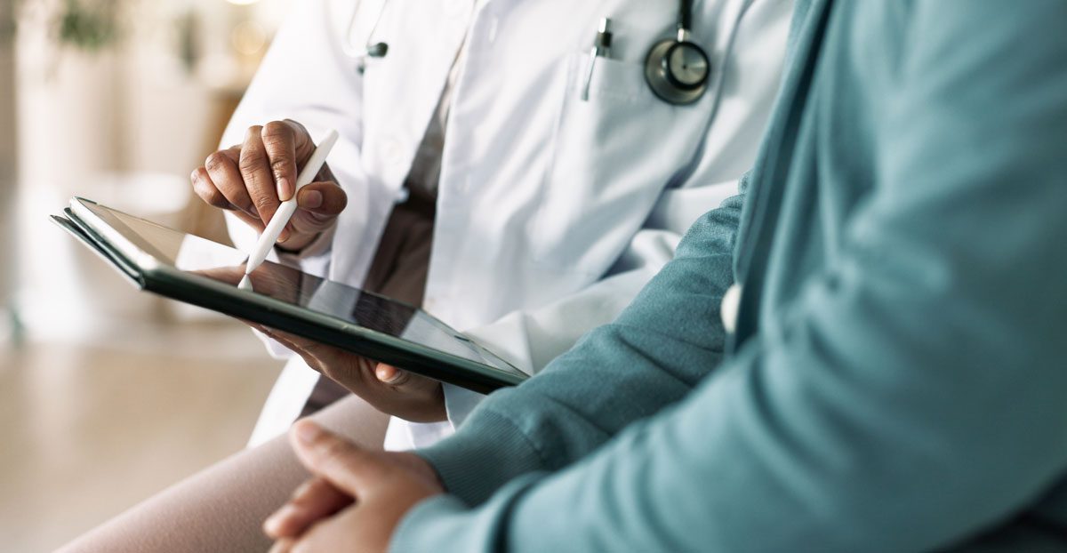 Doctor-explaining-medical-information-to-patient-on-tablet Doctor-explaining-medical-information-to-patient-on-tablet
