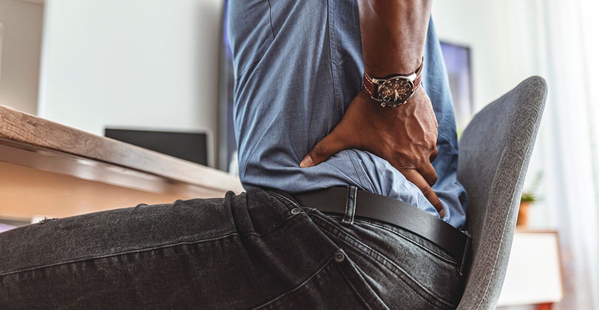 Man-holding-lower-back-pain-while-sitting-in-chai Man-holding-lower-back-pain-while-sitting-in-chai